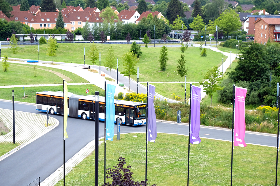 Ein Bus fährt auf der Straße vor der FH Bielefeld. Im Vordergrund sind die Flaggen vor dem FH-Hauptgebäude zu sehen.