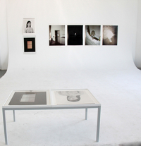 Weiße Wand mit Fotos, im Vordergrund zwei Bilder auf einem weißen Tisch.