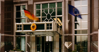 Eine Eingangstür über der die deutsche und die europäische Fahne wehen.