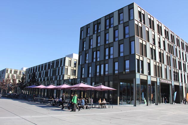 Das Hauptgebäude im Sonnenschein mit aufgespannten Sonnenschirmen an der Außengastronomie der Cafeteria.